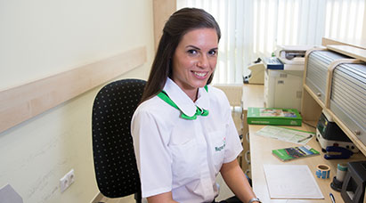 A képen egy mosolygó postai ügyintézőnő látható